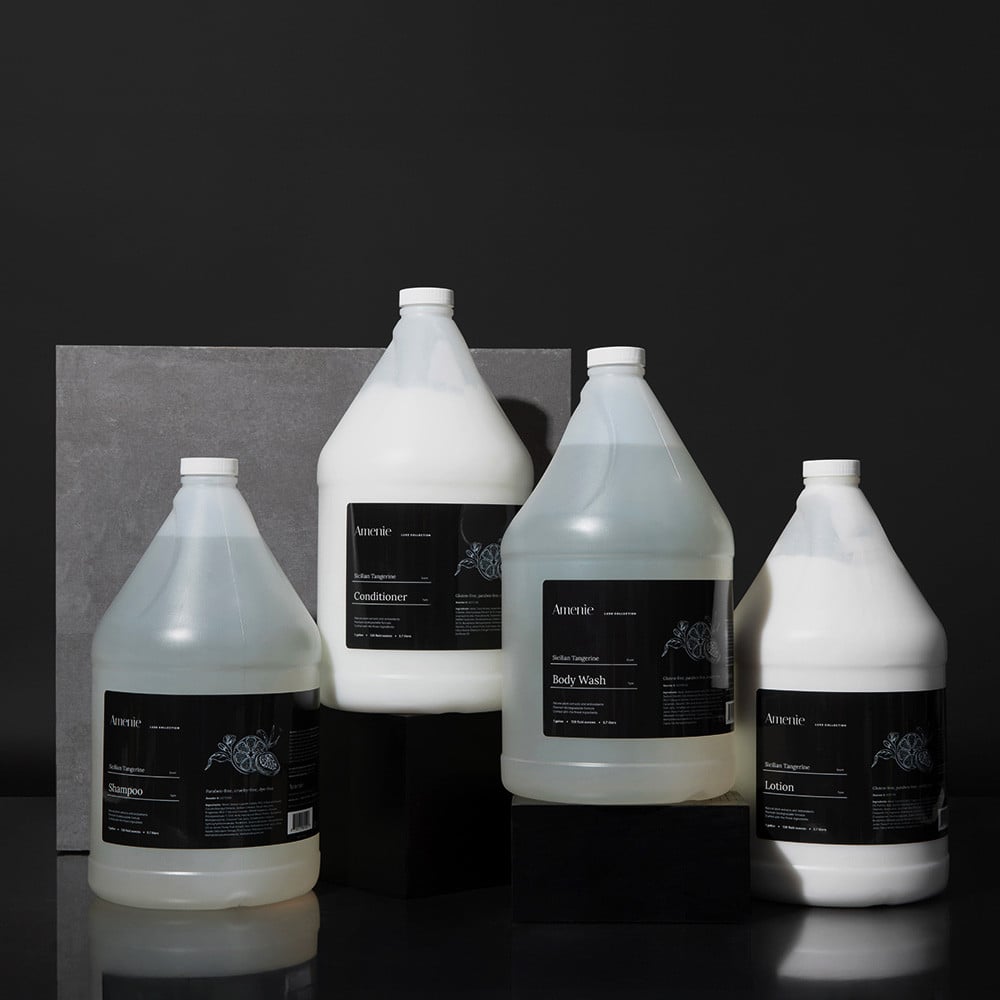 Amenie Sicilian Tangerine gallon-size collection with black labels on a dark stone background