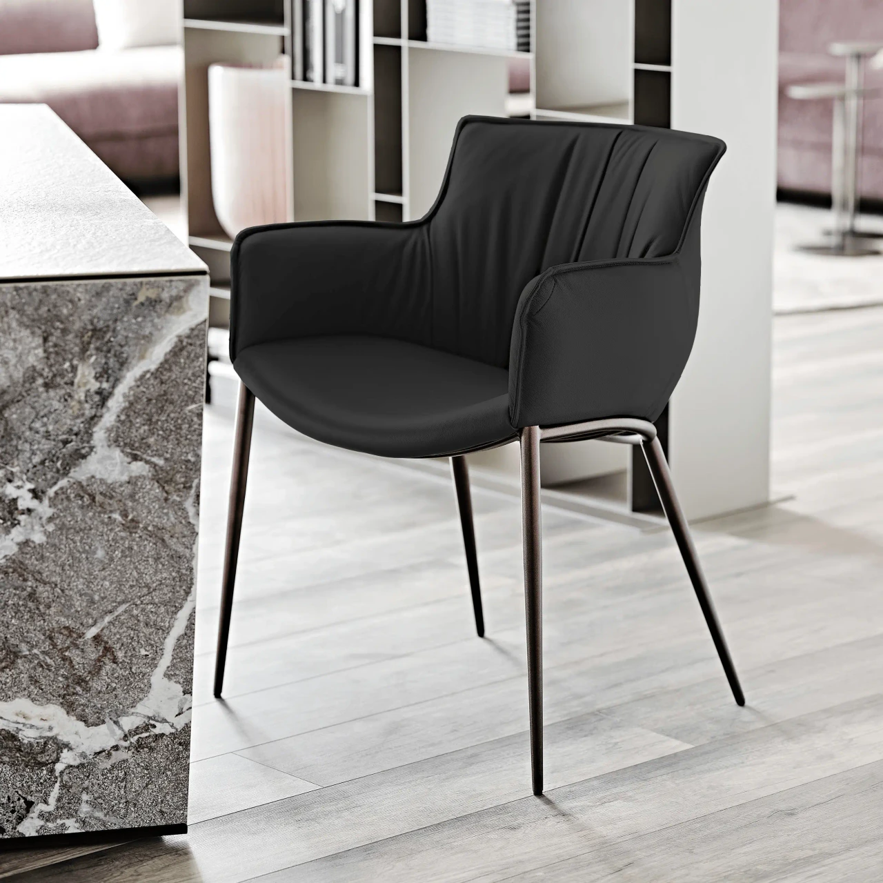 NERO || BRONZE EMBOSSED STEEL - Modern black leather armchair with slim metal legs and vertical stitching, shown from a three-quarter side angle.