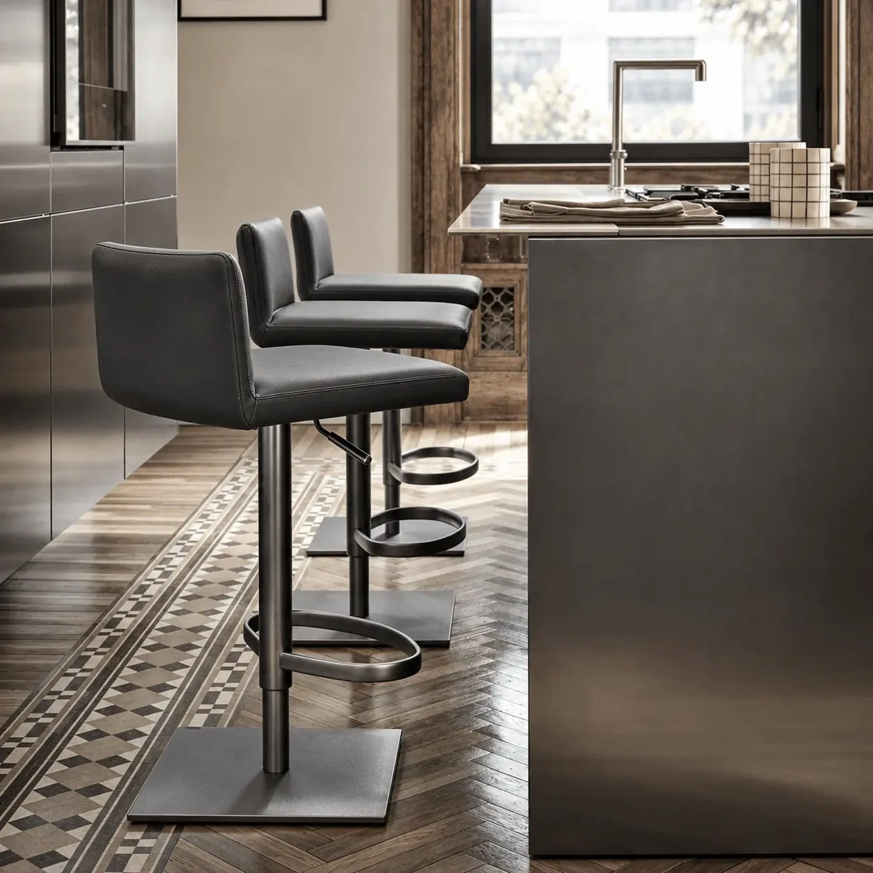 GREY LEATHER - Three Frag Bella Gp adjustable bar stools in dark grey leather with glossy chrome frames in a modern kitchen, side view.