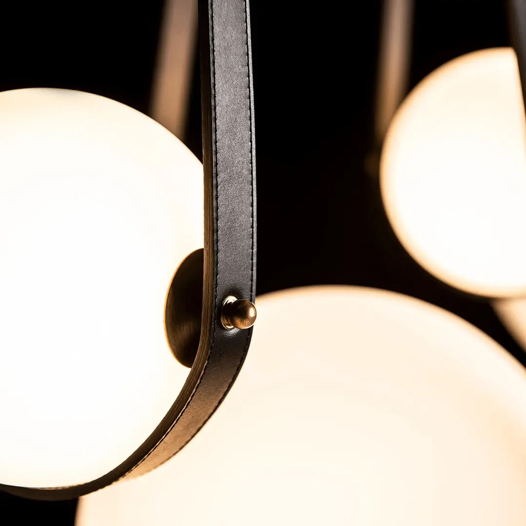 Closeup - Close-up of Derby Linear 4-light Fixture with opal glass, black leather strap, and antique brass accent.