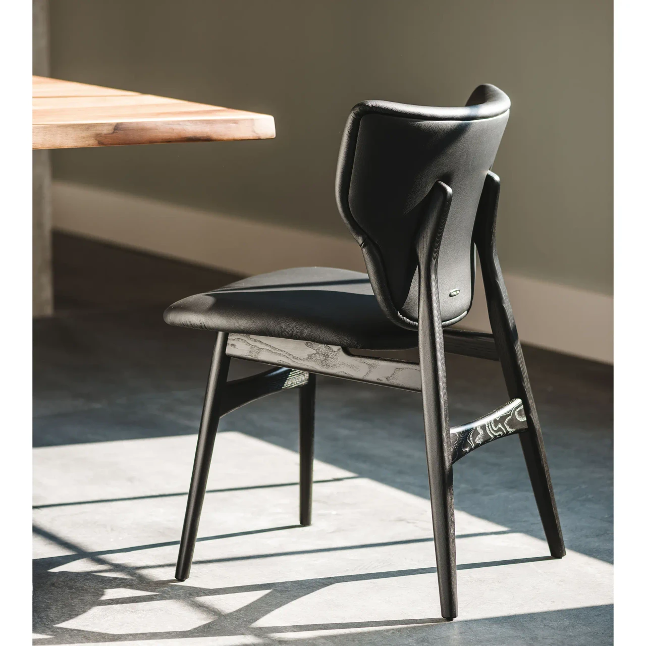 NERO SOFT LEATHER - Cattelan Dumbo Side Chair in Nero/Black Soft Leather and Black Stained Ashwood Frame, side view in a dining room setting.
