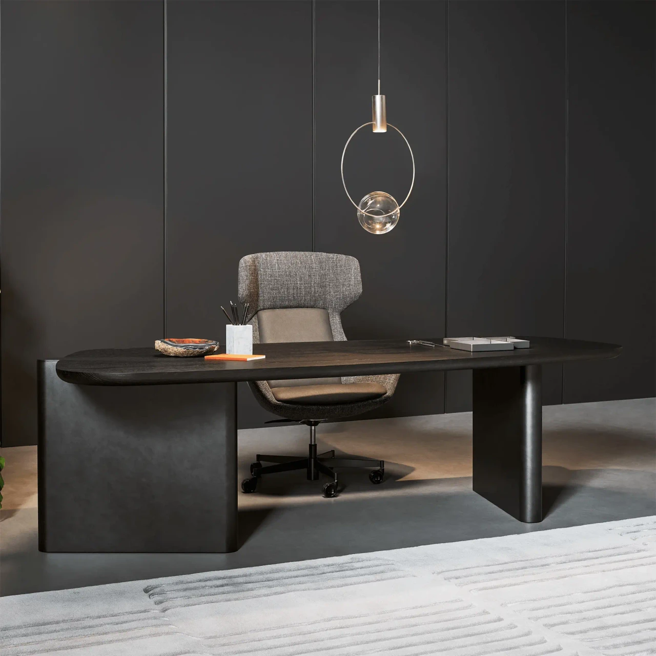 BRUSHED OAK - Modern black wooden executive desk with curved edges and grey office chair, front view against dark grey wall.