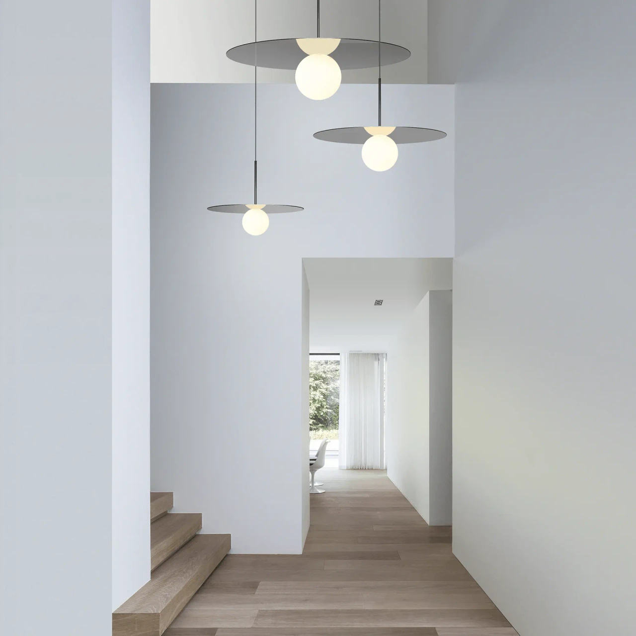 GUNMETAL || 12 IN - Pablo Bola Disc Pendant lights in gunmetal finish with opal glass globes in a modern white hallway, eye-level view.