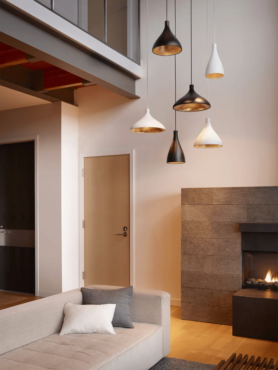 WHITE || 16 IN - Pablo Swell Pendant lights, matte white and black with brass interiors, hanging in a modern living room, eye-level view.