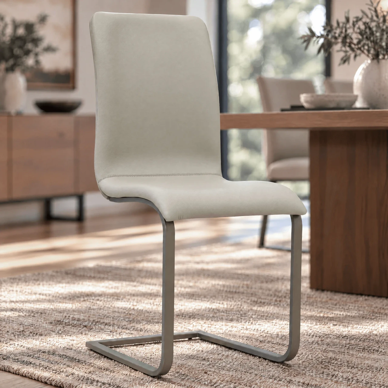 Toro Side Chair in beige leather with titanium powder coat frame, modern style, side view in a dining room setting.