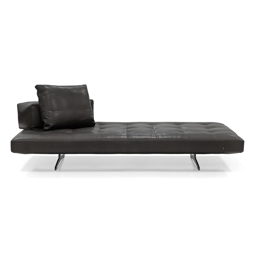 Modern dark brown leather daybed with tufted seat and two pillows, side view on white background.