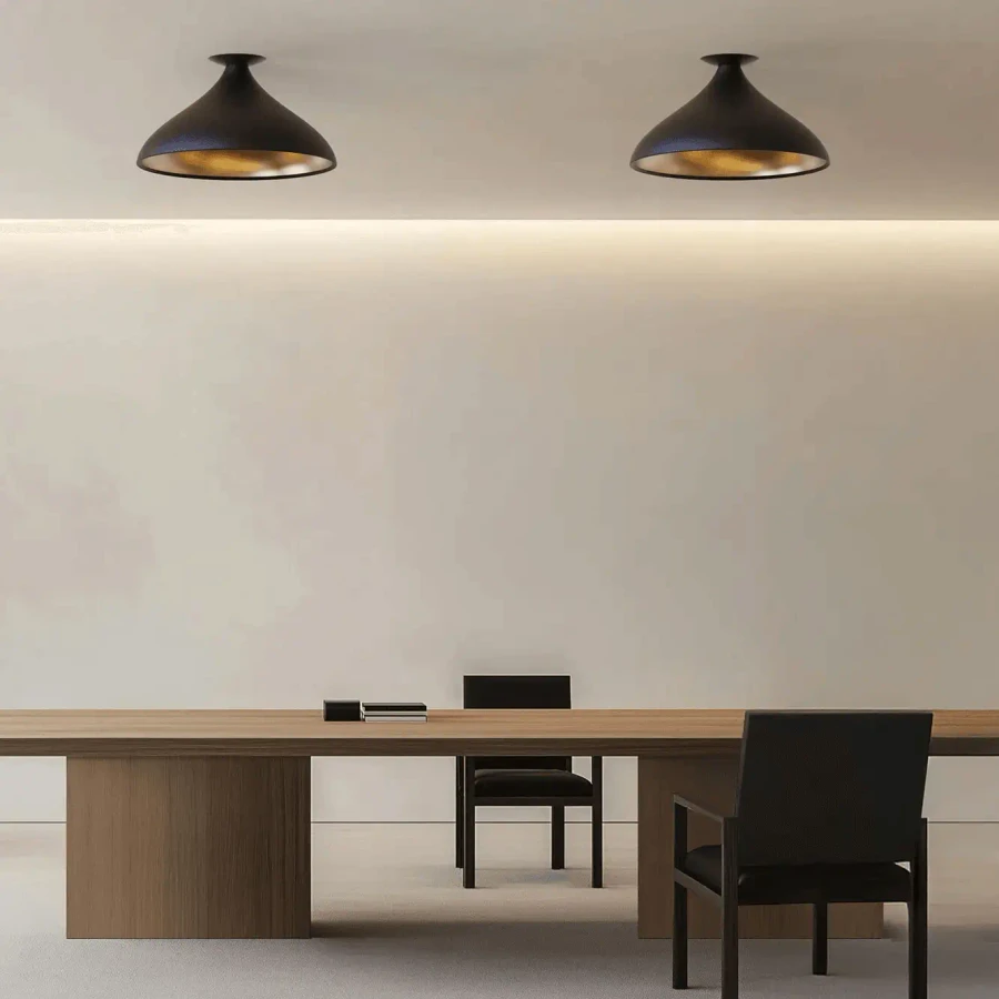 BLACK - Two Pablo Swell Xl Flush Lamps, matte black exterior, brass interior, in a modern office with a wooden table, front view.
