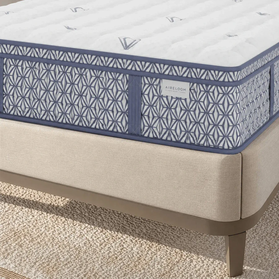 QUEEN - Bedroom close-up angle of Aireloom Euro Top Plush Mattress with blue geometric side pattern on a beige fabric bed frame.