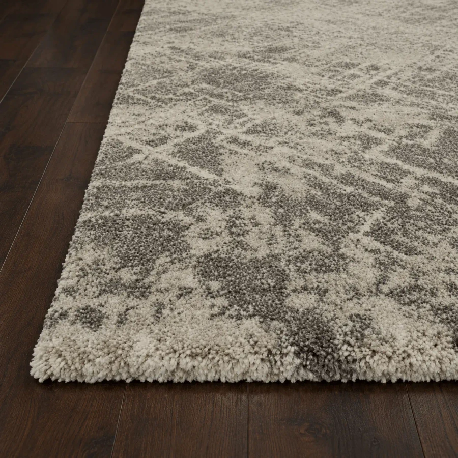 Close-up angle of Landscape Area Rug in Stone, power loomed polypropylene and acrylic with a textured pattern on dark wood