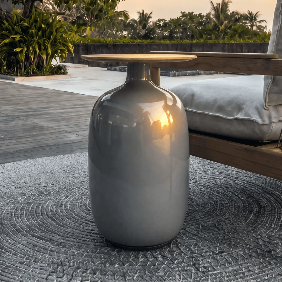 SMOKE - Gloster Blow High Side Table with smoke glazed ceramic base and natural teak top in outdoor patio setting, eye-level view.