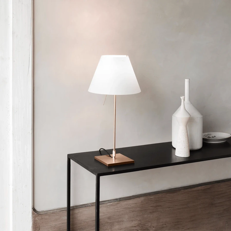 Costanzina Table Lamp with white polycarbonate shade and brass finish aluminum base on black console table in living room.