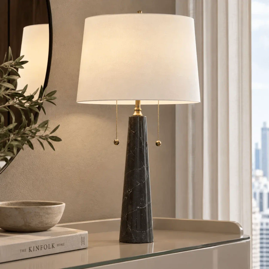Sidney Table Lamp in black marble and antique brass with off-white microfiber shade, side view in living room setting.