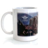 A ceramic mug stands on a clean white surface. On the mug is a painting of the monastery of Saint Catherine on Mount Sinai. 