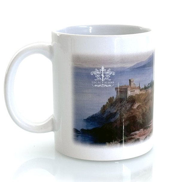 A ceramic mug stands on a clean white surface. On the mug is a printed a stylized landscape of the rocky coastline of Mount Athos. 