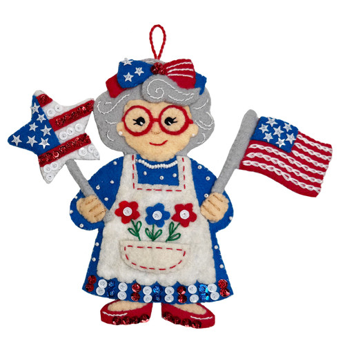 MerryStockings Mrs. Claus felt ornament in red, white, and blue, holding an American flag and star pinwheel, with a patriotic bow and stitched apron details.