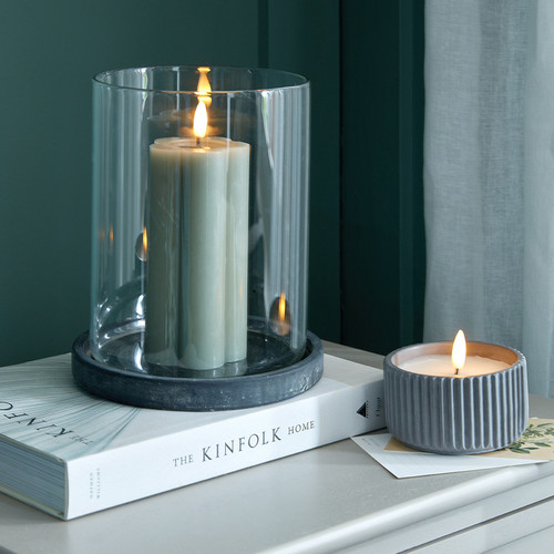 Amalfi Grey Large Hurricane Lantern with a lit candle, styled on a stack of books beside a matching ribbed candle holder