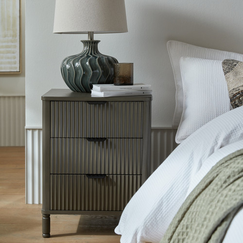 Reed 3 Drawer Bedside Table styled beside a bed with a table lamp and books on top