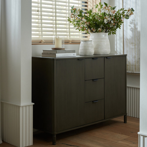 Reed 3 Drawer 2 Door Cabinet styled beside a window with vases, books, and a candle