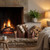 Copper finish logs and kindling buckets with matchstick holder resting on a stone hearth beside a lit fireplace, styled with a plant and lamp