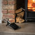 Antique pewter effect hearth tidy set resting on a wooden hearth beam beside a stacked log pile and lit fireplace