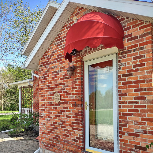 A vibrant red fabric awning in a dome shape, installed above the front door of a quaint residential home, adding a pop of color to the facade.