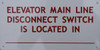 ELEVATOR MAIN LINE DISCONNECT SWITCH IS LOCATED AT  (ALUMINUM S ) WHITE Building  sign