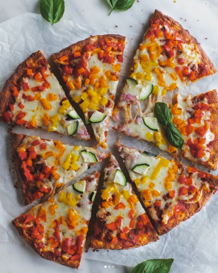 Sliced vegetable pizza topped with peppers, zucchini, and basil on parchment paper