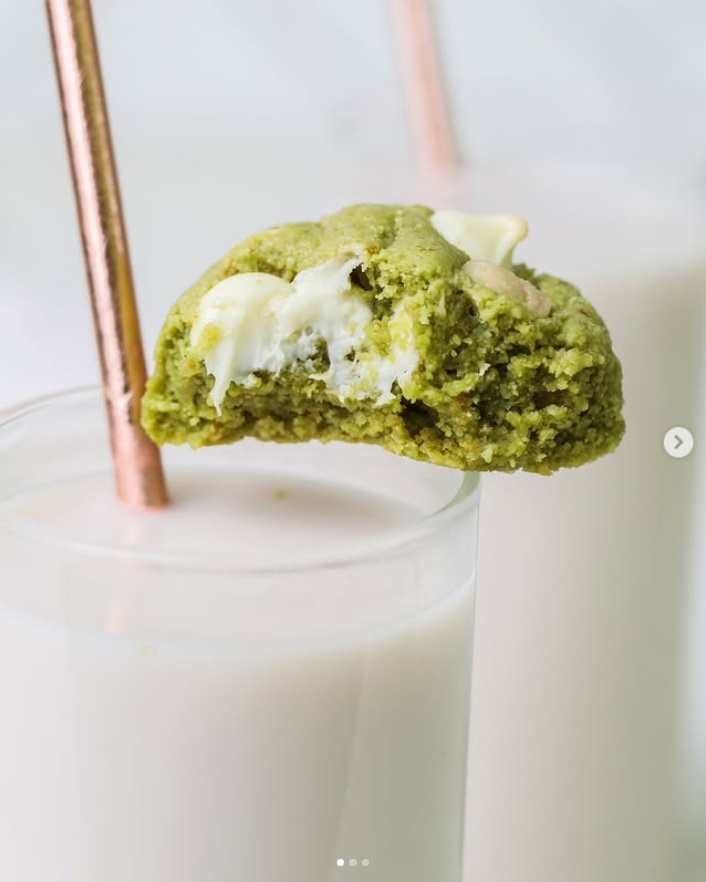 Green matcha cookie with white chocolate chips resting on a glass of milk with a copper straw