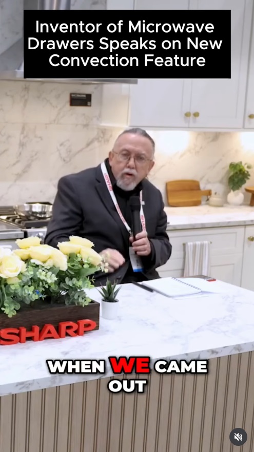 Video still of the inventor of the microwave drawer speaking into a microphone in a white marble kitchen