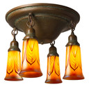 A traditional, Victorian or transitional Craftsman style ceiling light fixture with an aged patina finish and four hanging lights. They feature illuminated, trumpet-shaped blown glass shades with a red feather design.