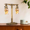  A stout and burly Arts & Crafts or Craftsman table lamp with an aged brass finish and curvy, blown glass shades placed under a houseplant on a credenza or sideboard.