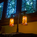  A beefy, English Arts & Crafts style lantern with delicate cherry blossom blown glass shades sits in front of leaded glass windows in a historic home.