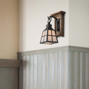  A short, wall mounted sconce lantern made with quarter sawn oak like Stickley furniture. The fixture is mounted on a metal hook with an oil rubbed bronze finish and a metal-framed glass shade with iridescent glass. It is installed in a living room with barn doors and a fireplace.