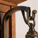  Metal hook detail of a tall, wall mounted sconce lantern made with quarter sawn oak like Stickley furniture. The fixture is mounted on a metal hook with an aged brass finish, turn key socket and a curvy, blown glass cherry blossom shade.
