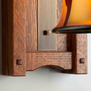  Bottom wall plate detail of a tall, wall mounted sconce lantern made with quarter sawn oak like Stickley furniture. The fixture is mounted on a metal hook with an aged brass finish, turn key socket and a curvy, blown glass cherry blossom shade.