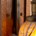  Wall plate brackets detail of a tall, wall mounted sconce lantern made with quarter sawn oak like Stickley furniture. The fixture is mounted on a metal hook with an aged brass finish, turn key socket and a curvy, blown glass cherry blossom shade.