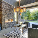  A rustic copper chandelier hangs above the seating area of a a back patio with a stone fireplace and linear, wicker furniture.