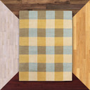  A Mid-Century Americana hand-knotted wool rug featuring a classic Madras plaid or large-scale checkered pattern. The design uses a palette of butter yellow, sky blue, taupe, and cream. It is against a background of flooring samples.
