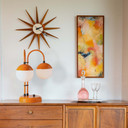  A mid-century lamp with an orange finish and two white globes sits on a credenza with modern art and accents.