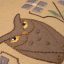  Closeup photo of a dark linen beige throw pillow featuring a embroidered design of petite owl artwork and tree branches.