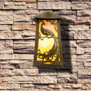  A flush mounted, art nouveau wall sconce light with an aged patina finish, glowing glass and peacock filigree installed on a stone facade wall.