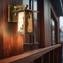  A rustic, artistic arm mounted wall sconce light fixture with a peaked roof, dragonfly artwork, an aged patina finish and warm white glass installed on an exterior wall of a home.