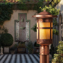  A Spanish Colonial Revival post mounted light fixture with a raw copper finish in front of an outdoor wall fountain and black and white tile floor.