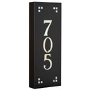  Angled view of a solid brass, vertically oriented illuminated house number plaque with a three number address, a satin black finish, warm-toned glass and corner glass accents.
