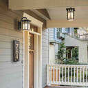  A solid brass, vertically oriented illuminated house number plaque with a three number address, a bronze finish, warm glass and corner glass accents installed next to the front door of a suburban Craftsman style home. There are a matching sconce and pendant lantern above the door.