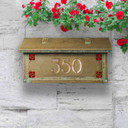  A Craftsman style mailbox featuring the Hunter Rose (sometimes called the Mackintosh Rose) as corner design accents. The mailbox has an aged patina finish and house address numbers backed by iridescent glass. It's installed on a stone wall under climbing red flowers.