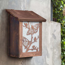  A small vertical mailbox against a concrete wall. It's made from copper and white art glass and features butterfly artwork.