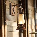  An antique-style hanging lantern sconce with a glowing frosted glass shade, mounted on a rustic weathered wood plank wall.