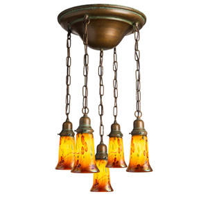  A traditional, Victorian or transitional Craftsman style chandelier with an aged patina finish and five lanterns on chains. The lanterns have illuminated, trumpet-shaped blown glass shades with a poppy design.