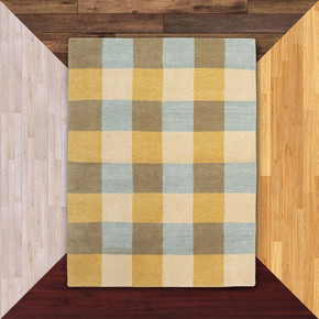  A Mid-Century Americana hand-knotted wool rug featuring a classic Madras plaid or large-scale checkered pattern. The design uses a palette of butter yellow, sky blue, taupe, and cream. It is against a background of flooring samples.